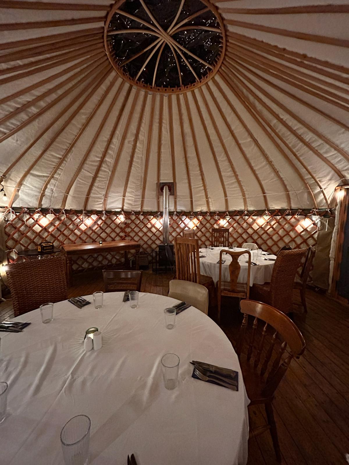 Round tables dressed for dinner inside the garden yurt