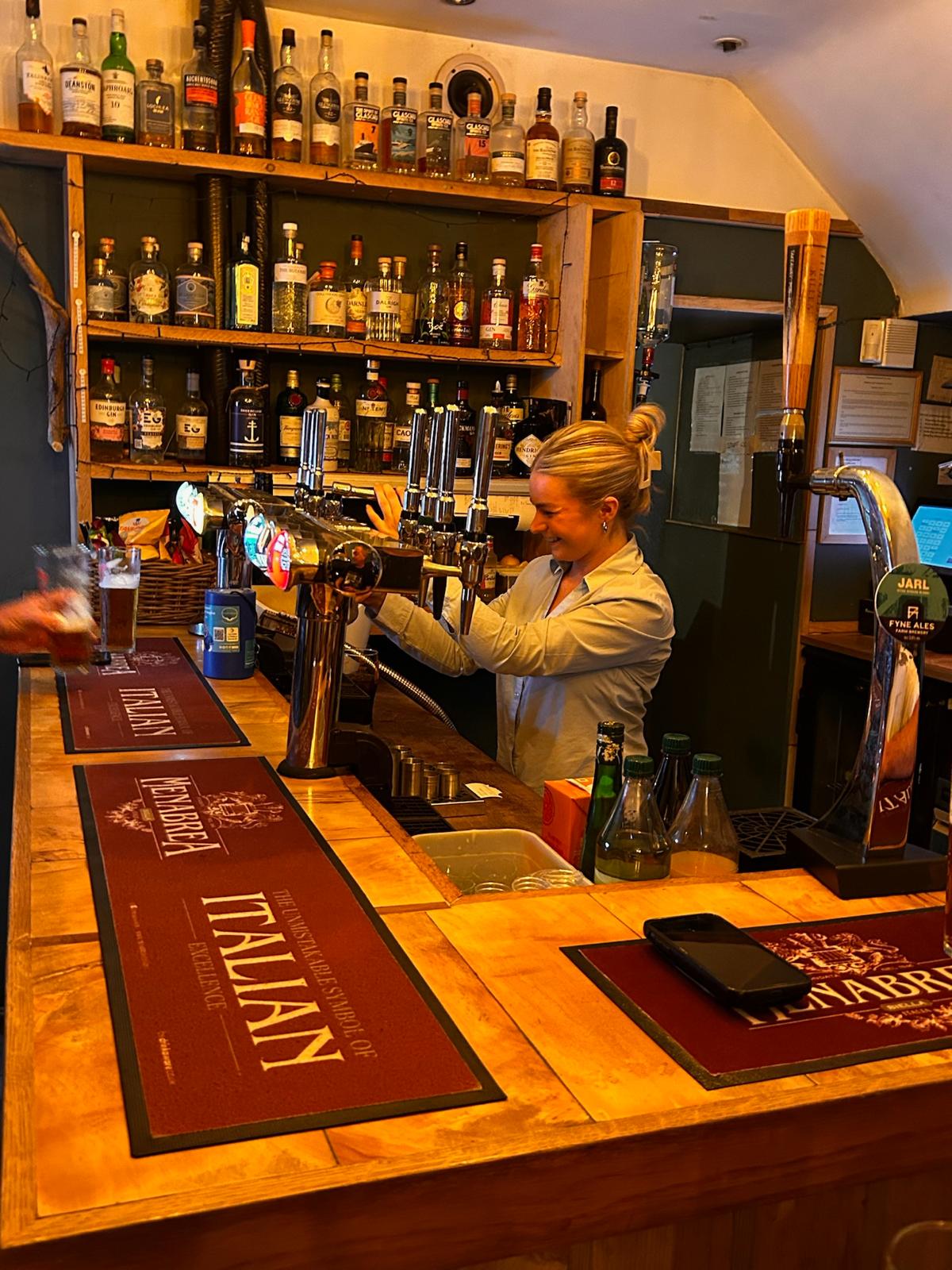 A smiling bartender pulling a pint behind the bar, lined with spirits and beer taps