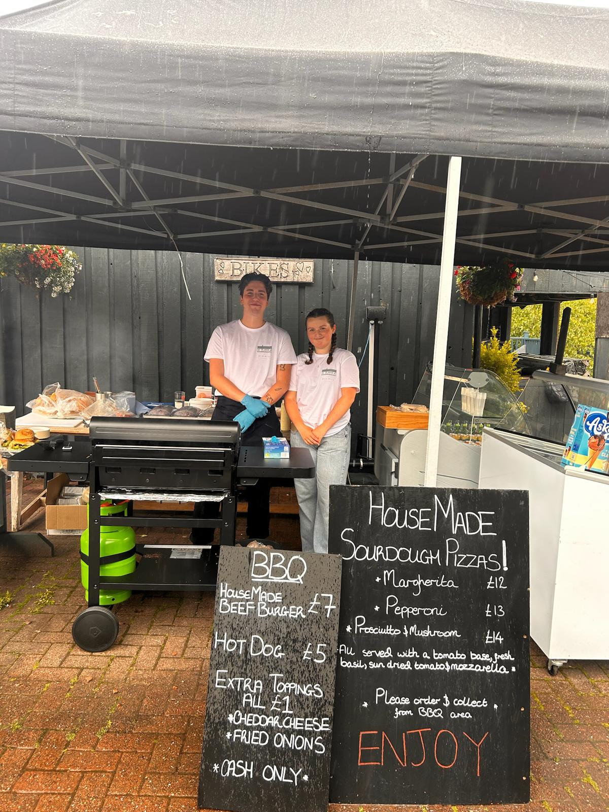 Two cooks running the outdoor food stand, burger buns and grilling laid out on the barbecue
