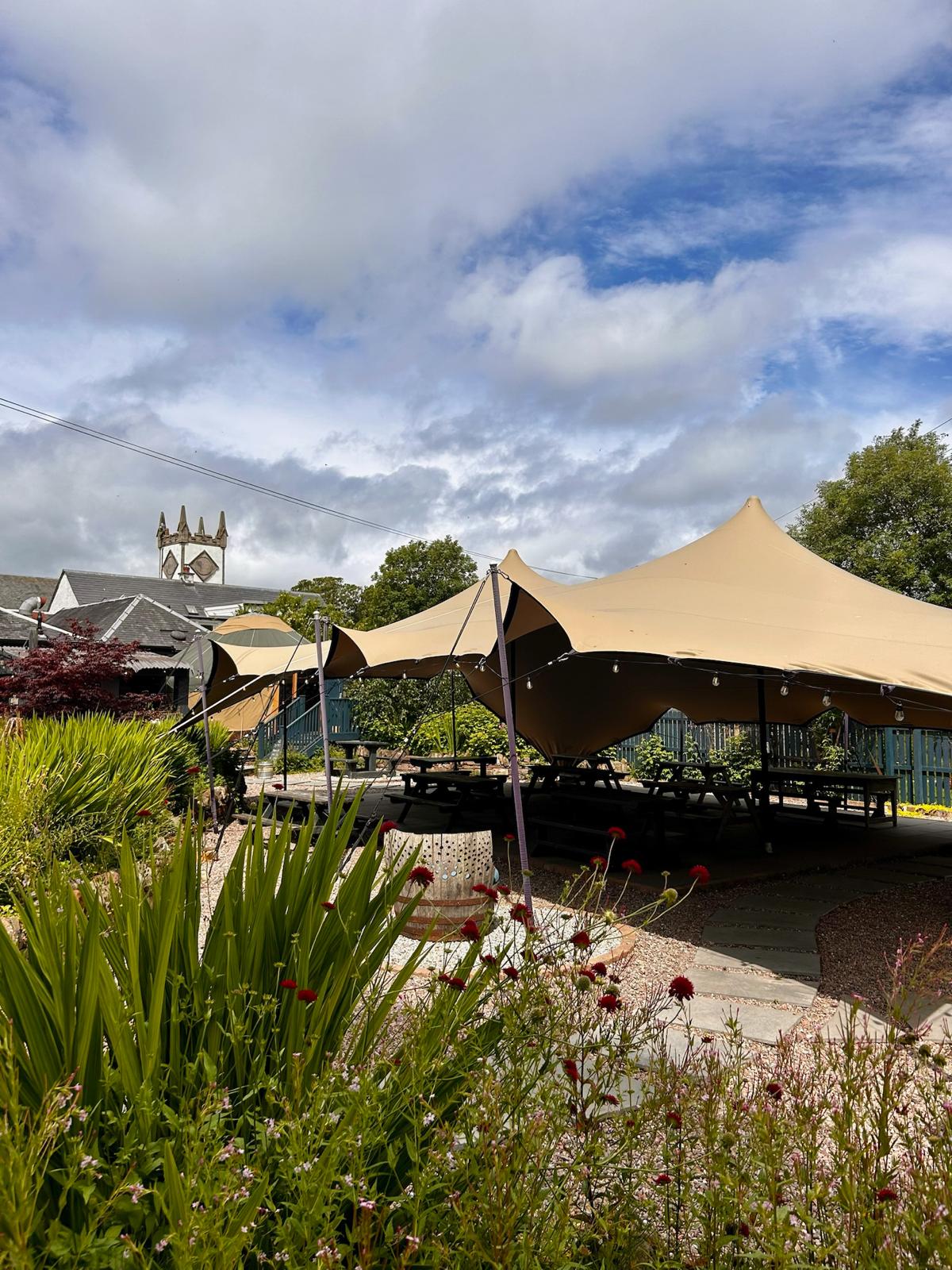 A canopy tent shading the garden picnic benches, the church tower rising beyond