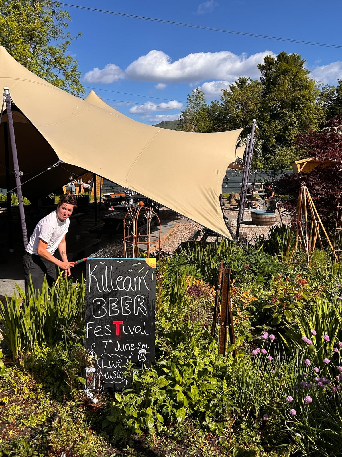 Someone watering the plants beside a chalkboard sign in the marquee beer garden