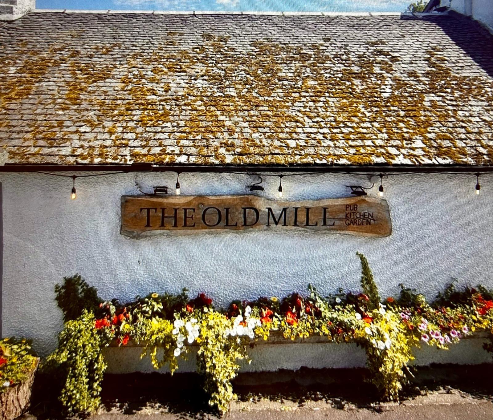 The whitewashed front of The Old Mill, its kitchen garden sign framed by flower planters