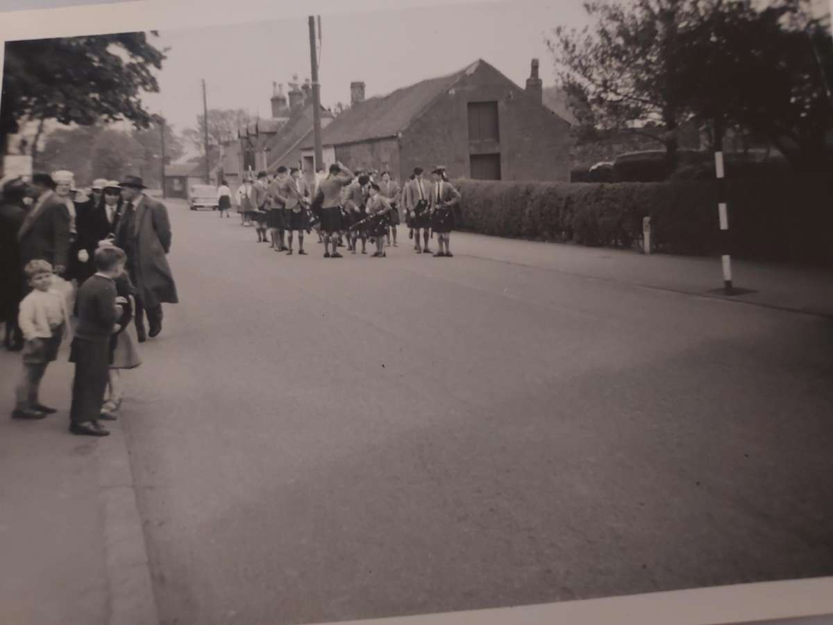 A pipe band marching through Killearn village past The Old Mill