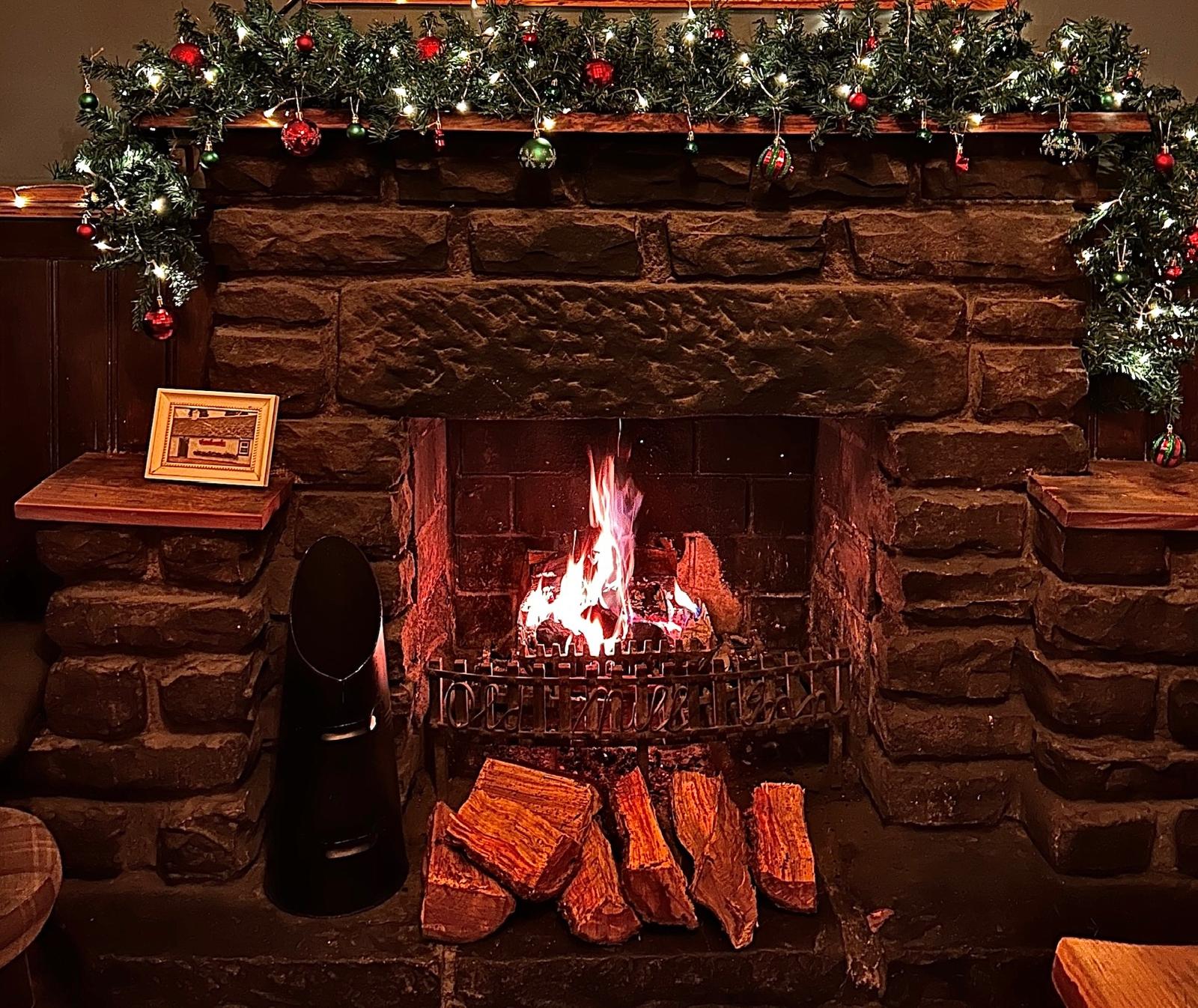 The stone hearth decorated for Christmas with a roaring log fire